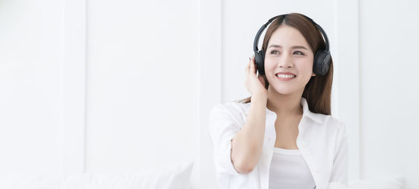 Portrait of a smiling young woman standing against white wall