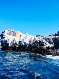 Scenic view of sea by mountain against clear blue sky