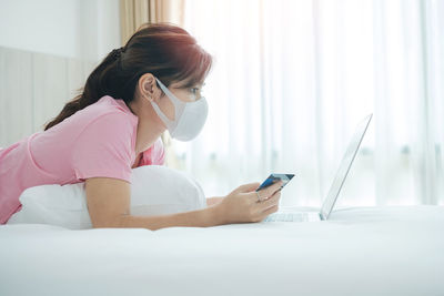 Side view of woman wearing mask using laptop at home