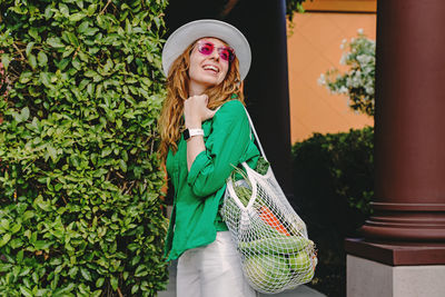 Young woman holding a mesh bag with veggies on her shoulder. modern lifestyle, grocery shopping