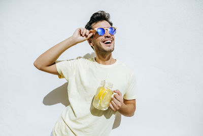 Young an with sunglasses and lemonade in front white wall