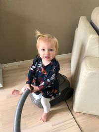 High angle portrait of cute baby girl sitting on vacuum cleaner at home