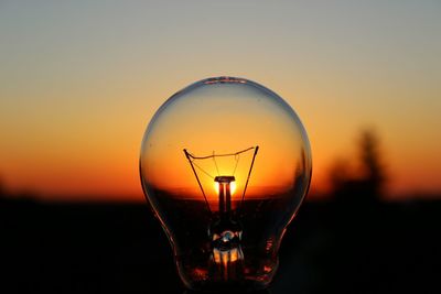 Close-up of light bulb against sky during sunset