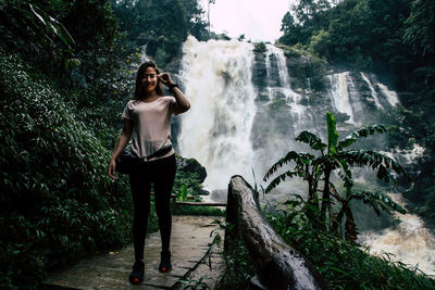 Portrait of young woman standing against waterfall