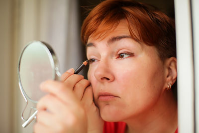 Close-up of woman applying eyeliner while looking at mirror at home 