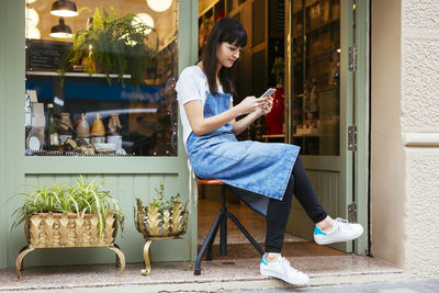 Woman sitting on stool using cell phone at entrance door of a store