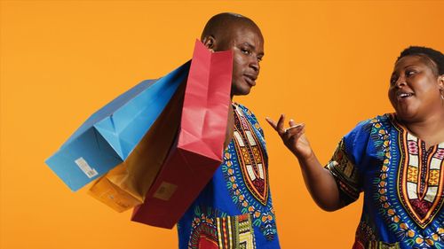 Side view of couple holding shopping bags against yellow background