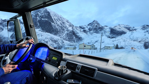 Midsection of person driving truck against snowcapped mountains