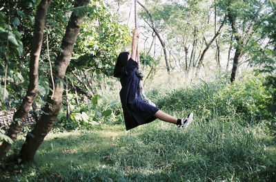 Young woman swinging against trees at forest