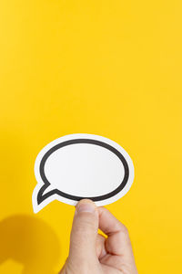 Close-up of hand holding paper against yellow background