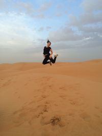 Full length of woman jumping on sand dune