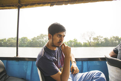 Young man sitting in boat on lake against sky