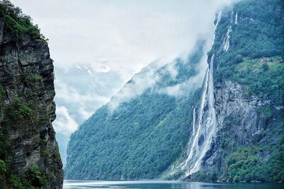 Waterfall on mountain by river against sky 