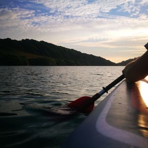 Person holding boat in lake against sky during sunset