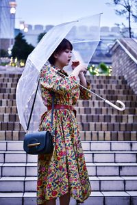 Young woman holding umbrella standing against built structure