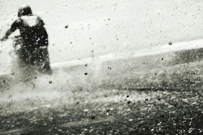 Rear view of woman seen through wet glass window in rainy season