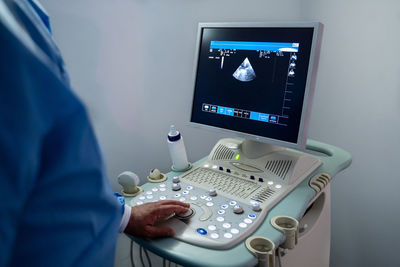 High angle of crop person in medical uniform using special ultrasound equipment while performing diagnosis disease of patient in light room of modern hospital