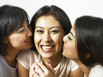 Happy friends kissing woman while siting on sofa at home