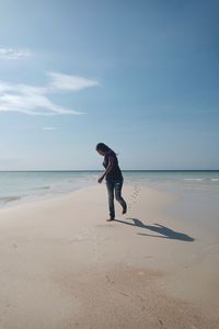 Rear view of woman standing at beach against sky