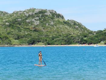 Woman paddleboarding in sea against mountains