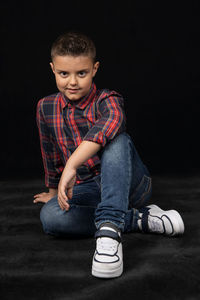 Portrait of boy sitting against black background