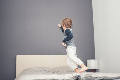 Full length of man sitting on bed against wall at home