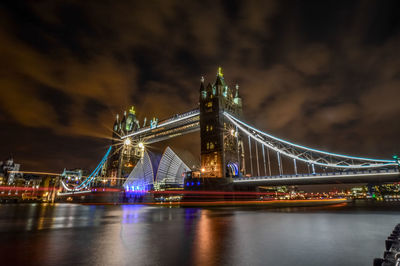 Illuminated tower bridge over river against sky at night