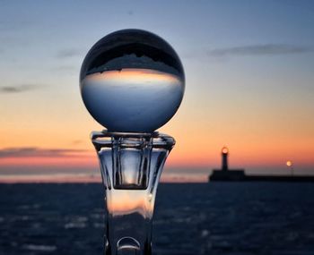 Sunrise through a lensball on a crystal stand with lighthouse in the background 