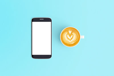 Directly above shot of coffee cup and mobile phone on blue background