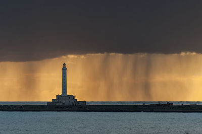 Lighthouse by sea against sky during sunset