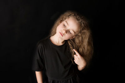 Portrait of teenage girl standing against black background