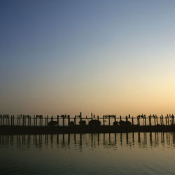 Silhouette pier in calm sea at sunset