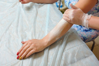 Cropped hand of beautician waxing woman