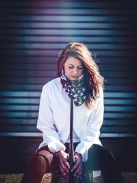 Woman holding baseball bat while sitting against shutter