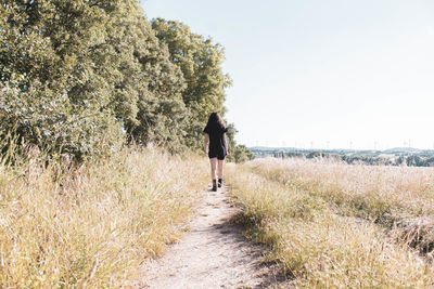 Rear view of person walking on footpath amidst field