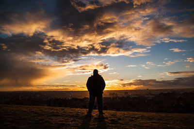 Rear view of silhouette man standing on field against cloudy sky