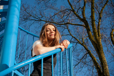 Low angle view of woman on railing against blue sky