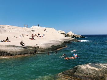 People on beach against clear blue sky