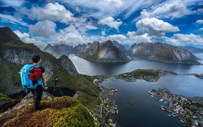 Rear view of man photographing mountains and lake against sky