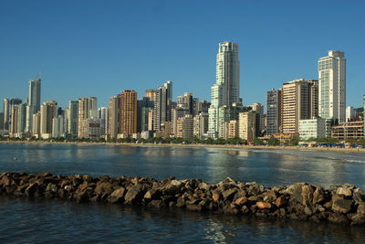 City skyline by sea against clear sky