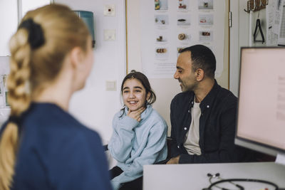 Smiling girl explaining to doctor while sitting with father during visit in clinic