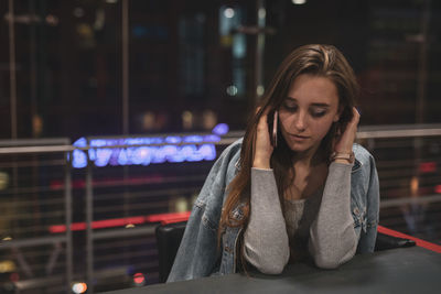 Beautiful young woman talking on mobile phone while sitting on table at night