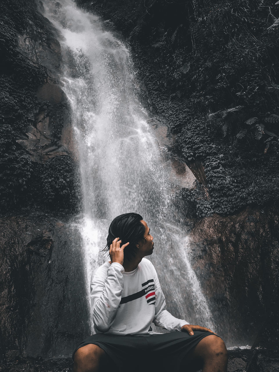 MAN SITTING ON ROCK LOOKING AT WATERFALL