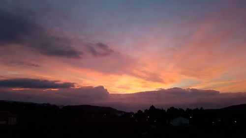 Scenic view of silhouette houses against dramatic sky during sunset