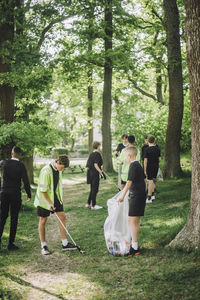 Full length of male friends collecting plastic in garbage bag