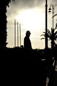 Silhouette man sitting by plants against sky during sunset