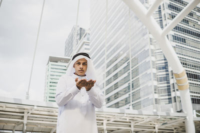 Portrait of man traditional clothing standing with hands cupped against buildings