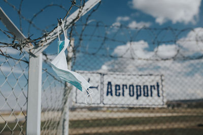 Warning sign on fence against sky