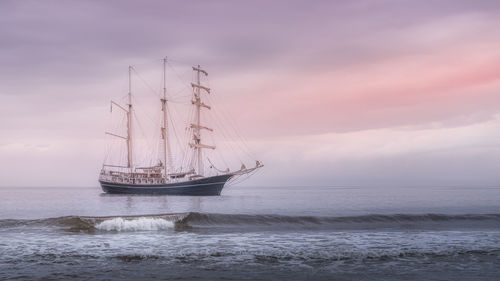 Rolling wave in front of tall ship covered in haze, anchored near northern ireland coast