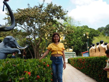 Portrait of smiling young woman standing by plants against trees